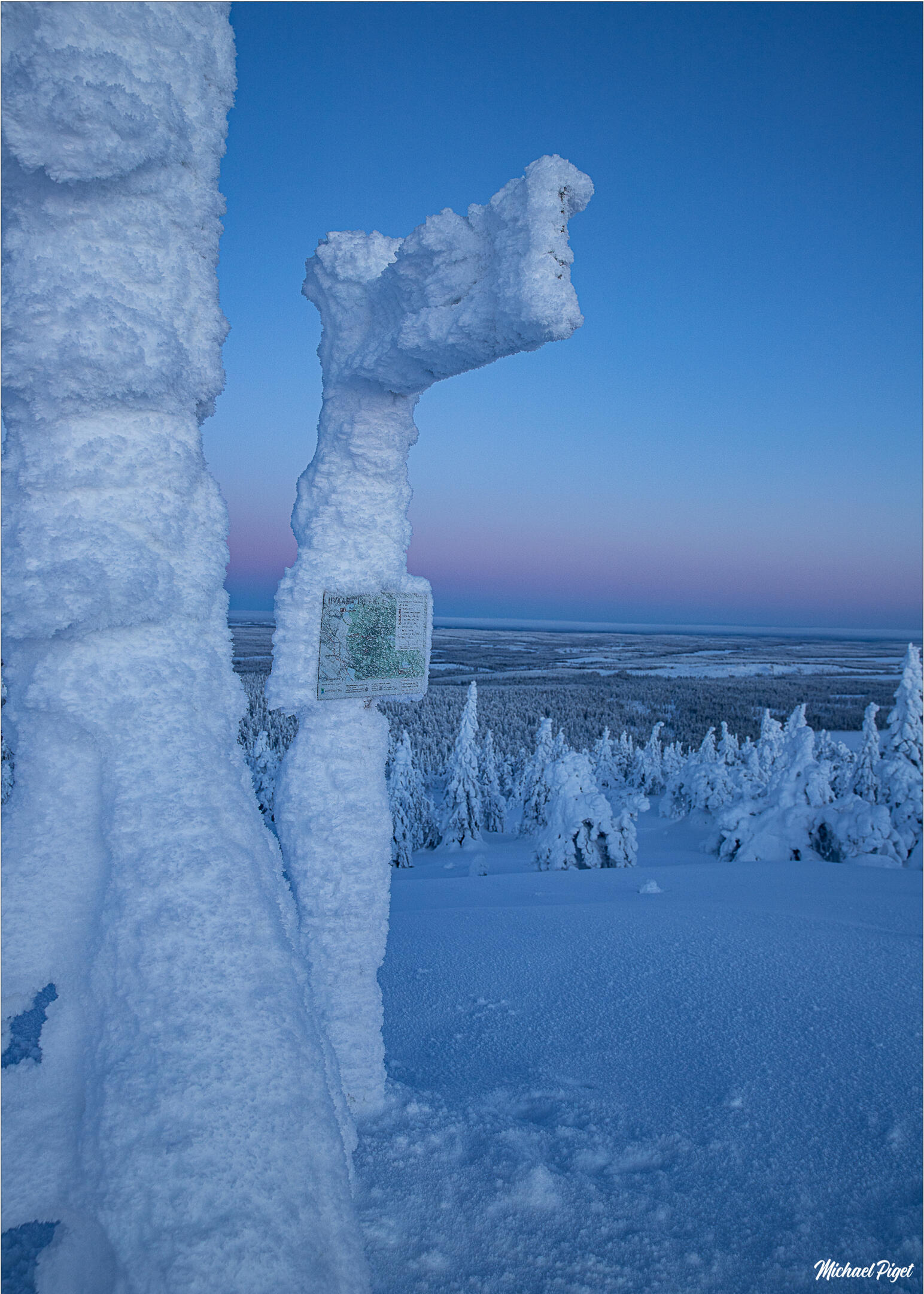 Panneau givré dans un paysage enneigé en Finlande sous un ciel bleu et rose au crépuscule